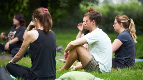 A group of people sitting quietly on the grass in a circle, engaged in a mindful outdoor session surrounded by greenery at the Nostell Nature Retreat.